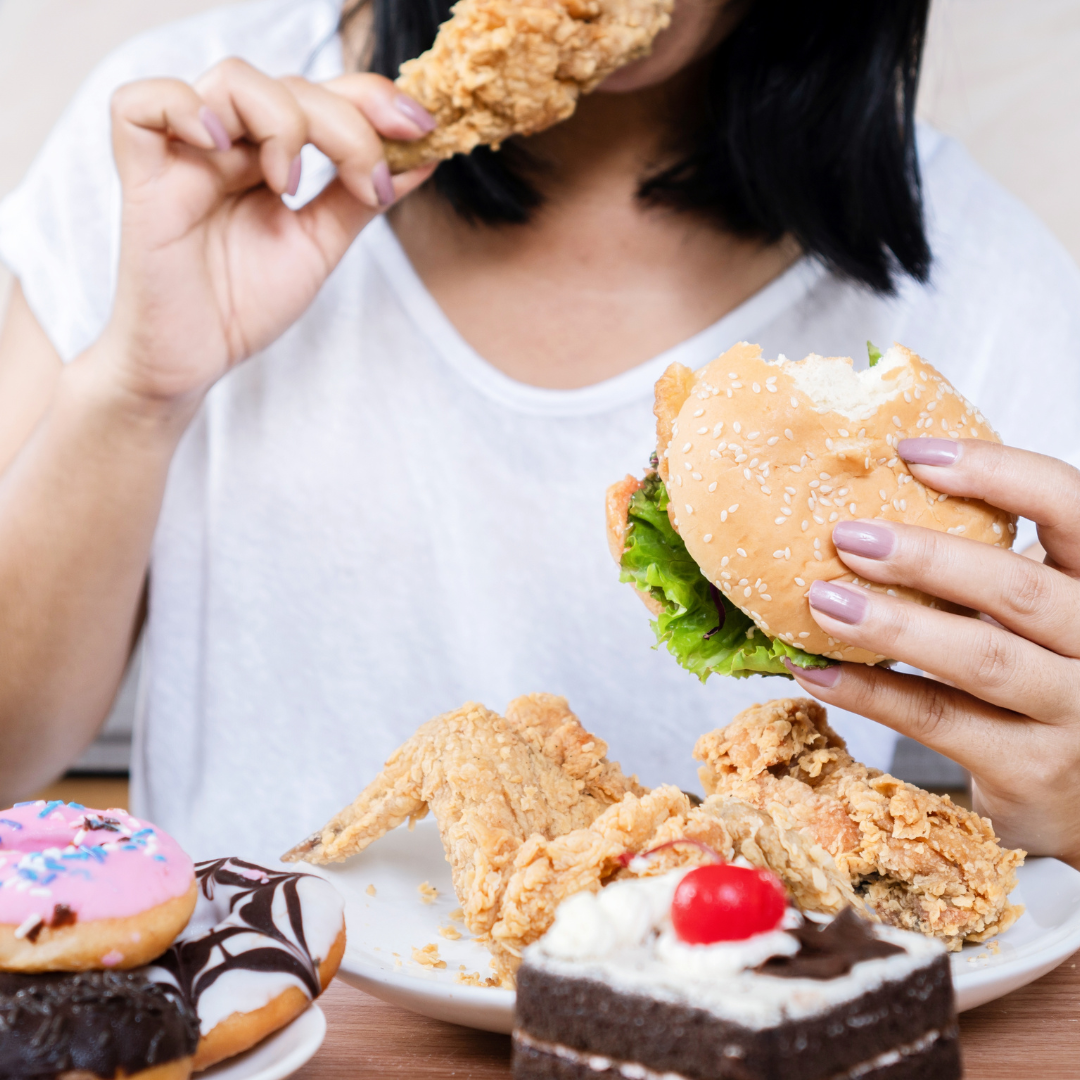 Pessoa consumindo hambúrguer e alimentos fritos em refeição ultraprocessada